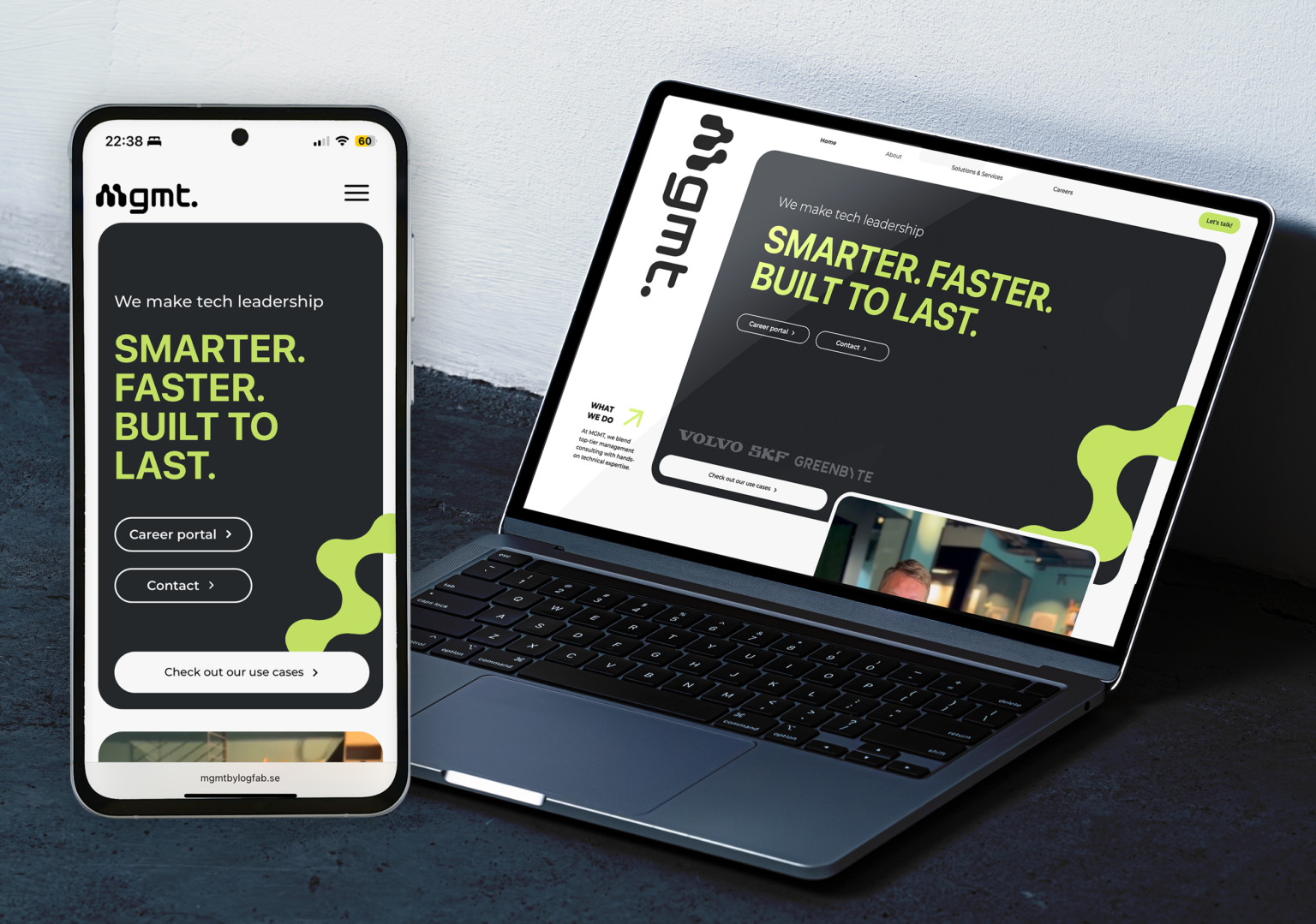 A mockup featuring a mobile and a desktop layout of Mgmts new website. The laptop is resting on a concrete surface and the mobile phone is a cutout.